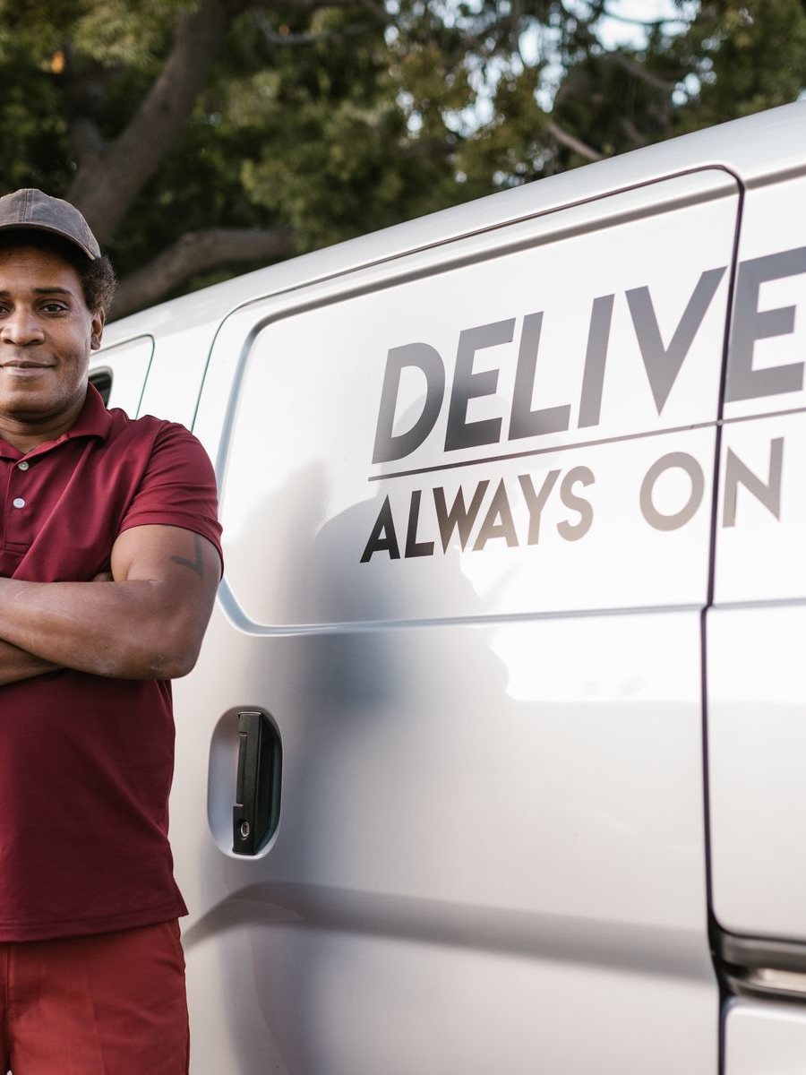 A delivery driver in a maroon polo stands beside his van