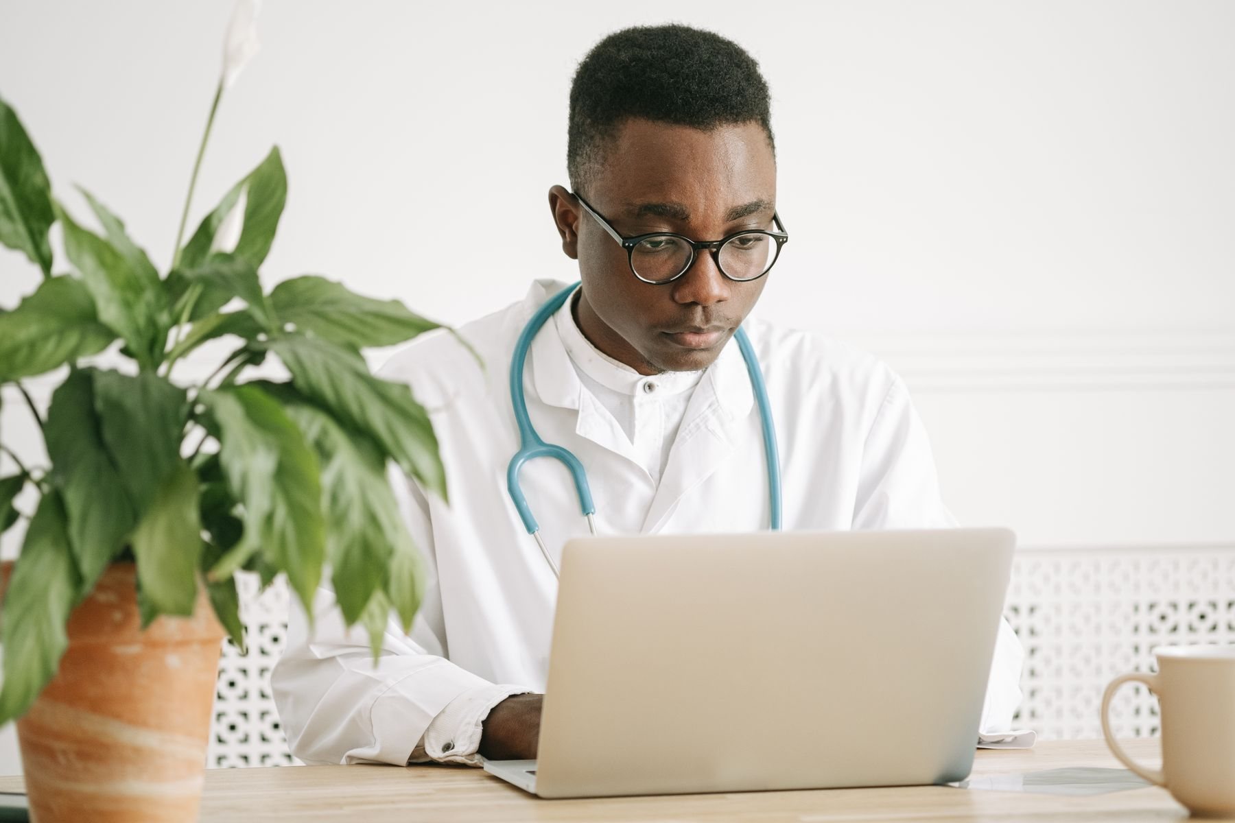 A doctor with a stethoscope works on his laptop