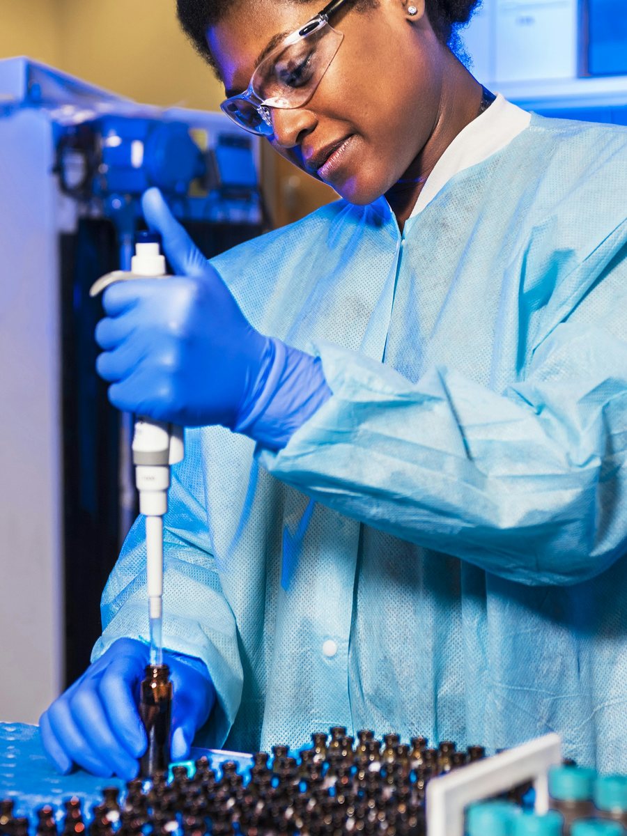 A laboratory technician in safety glasses pipettes a sample