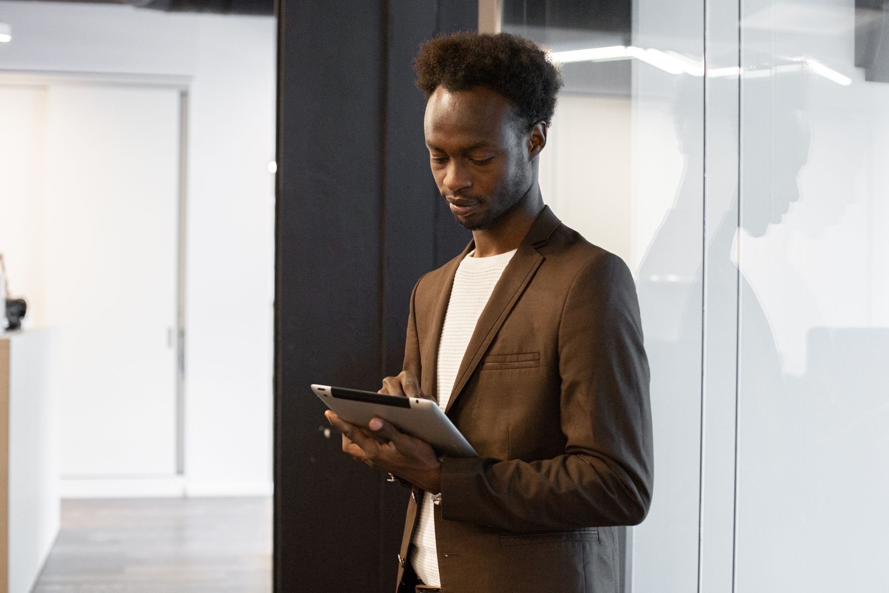 A hotel manager in a brown blazer reviews a tablet in a bright corridor