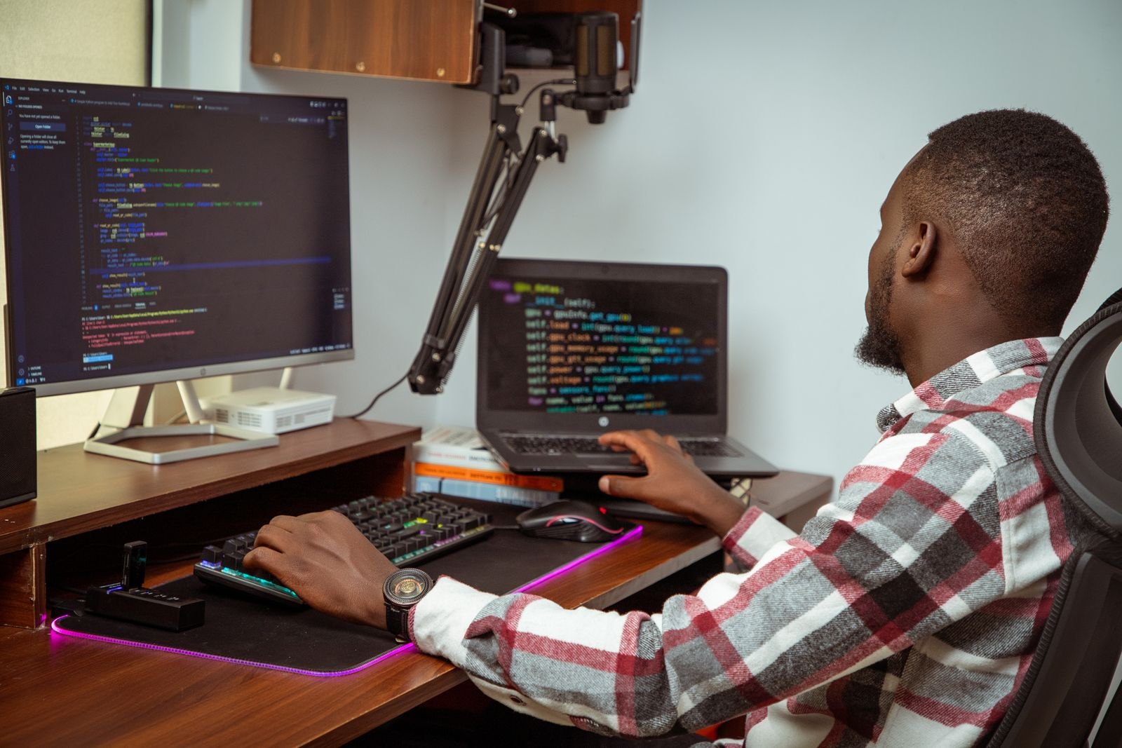 An engineer at his desk writing code, a monitor and a laptop in front of him.